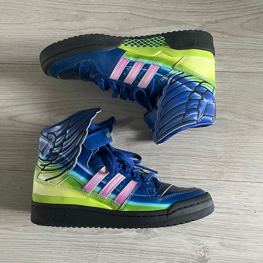 The Adidas Jeremy Scott Motorsport Wings 4.0 features a leather upper in blue with a gradient transitioning to green, accented by shock pink and light pink logo stripes. This high-top sneaker includes breathable perforations, a grippy rubber outsole, padded tongue, and signature Wings detailing at the collar. Released in 2022, the limited edition model comes with its original box and is crafted for comfort and style.