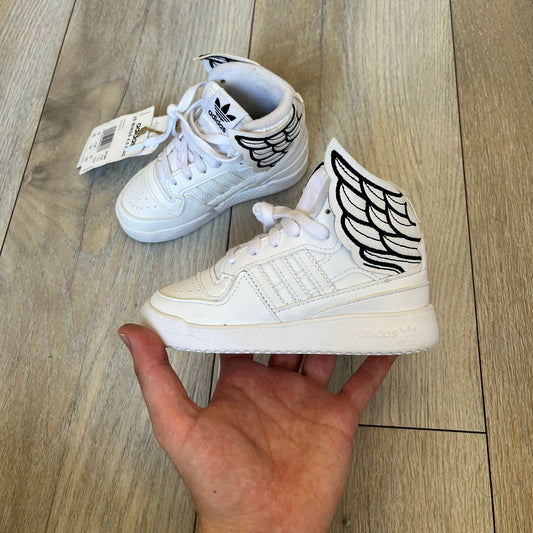 Adidas x Jeremy Scott Wings 4.0 Kids Sneakers were released on May 5, 2022. They feature white premium leather uppers with black Three Stripes, black heel tabs, and Jeremy Scott Wings branding. The high-top design includes a padded collar and tongue, along with a rubber herringbone outsole. One shoe is bigger than the other, making it primarily suitable as a display or collectible item.
