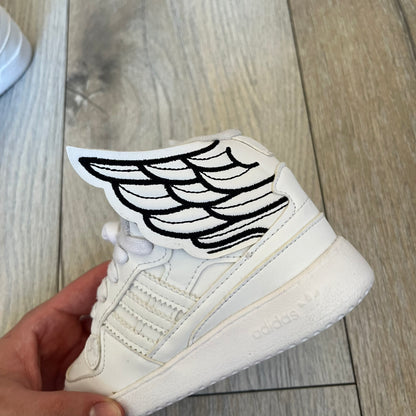Adidas x Jeremy Scott Wings 4.0 Kids Sneakers were released on May 5, 2022. They feature white premium leather uppers with black Three Stripes, black heel tabs, and Jeremy Scott Wings branding. The high-top design includes a padded collar and tongue, along with a rubber herringbone outsole. One shoe is bigger than the other, making it primarily suitable as a display or collectible item.
