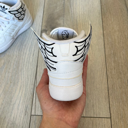 Adidas x Jeremy Scott Wings 4.0 Kids Sneakers were released on May 5, 2022. They feature white premium leather uppers with black Three Stripes, black heel tabs, and Jeremy Scott Wings branding. The high-top design includes a padded collar and tongue, along with a rubber herringbone outsole. One shoe is bigger than the other, making it primarily suitable as a display or collectible item.
