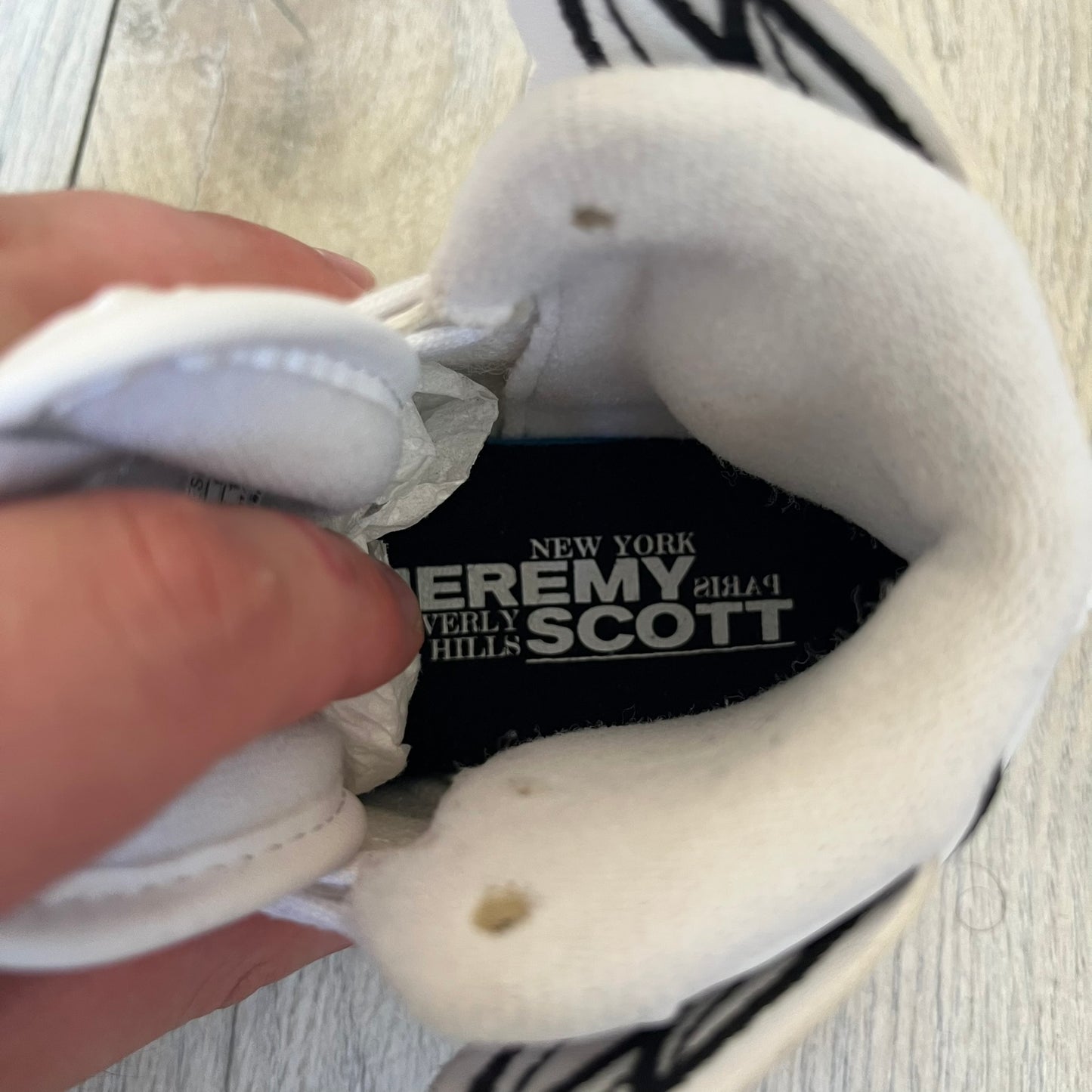 Adidas x Jeremy Scott Wings 4.0 Kids Sneakers were released on May 5, 2022. They feature white premium leather uppers with black Three Stripes, black heel tabs, and Jeremy Scott Wings branding. The high-top design includes a padded collar and tongue, along with a rubber herringbone outsole. One shoe is bigger than the other, making it primarily suitable as a display or collectible item.
