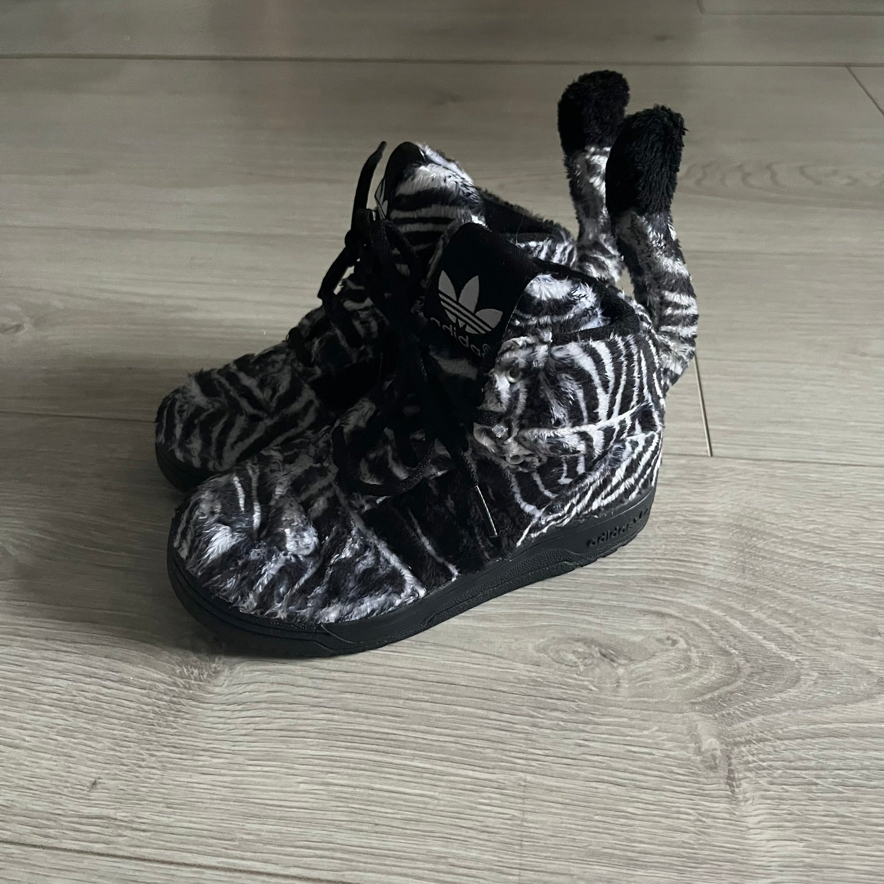 Adidas Jeremy Scott Zebra Black &amp; White Sneakers - Sample pair, Style G95749. High-top sneakers featuring black and white faux-fur zebra print, a 3D tail at the heel, rubber soles, and front lace closure. From the FW13 Jeremy Scott for Adidas collection, these iconic sneakers combine classic adidas design with signature crazy JS styling.