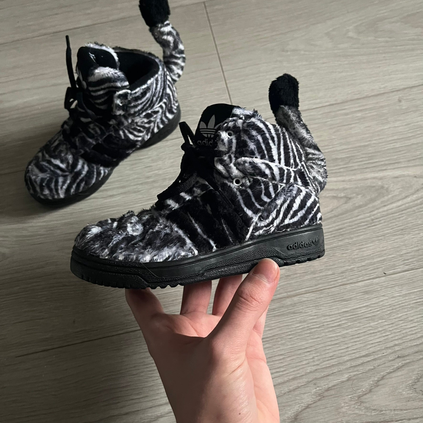 Adidas Jeremy Scott Zebra Black &amp; White Sneakers - Sample pair, Style G95749. High-top sneakers featuring black and white faux-fur zebra print, a 3D tail at the heel, rubber soles, and front lace closure. From the FW13 Jeremy Scott for Adidas collection, these iconic sneakers combine classic adidas design with signature crazy JS styling.