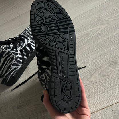 Adidas Jeremy Scott Zebra Black &amp; White Sneakers – Sample pair, Style G95749. High-top sneakers featuring black and white faux-fur zebra print, a 3D tail at the heel, rubber soles, and front lace closure. From the FW13 Jeremy Scott for Adidas collection, these iconic sneakers combine classic adidas design with signature crazy JS styling.&nbsp;