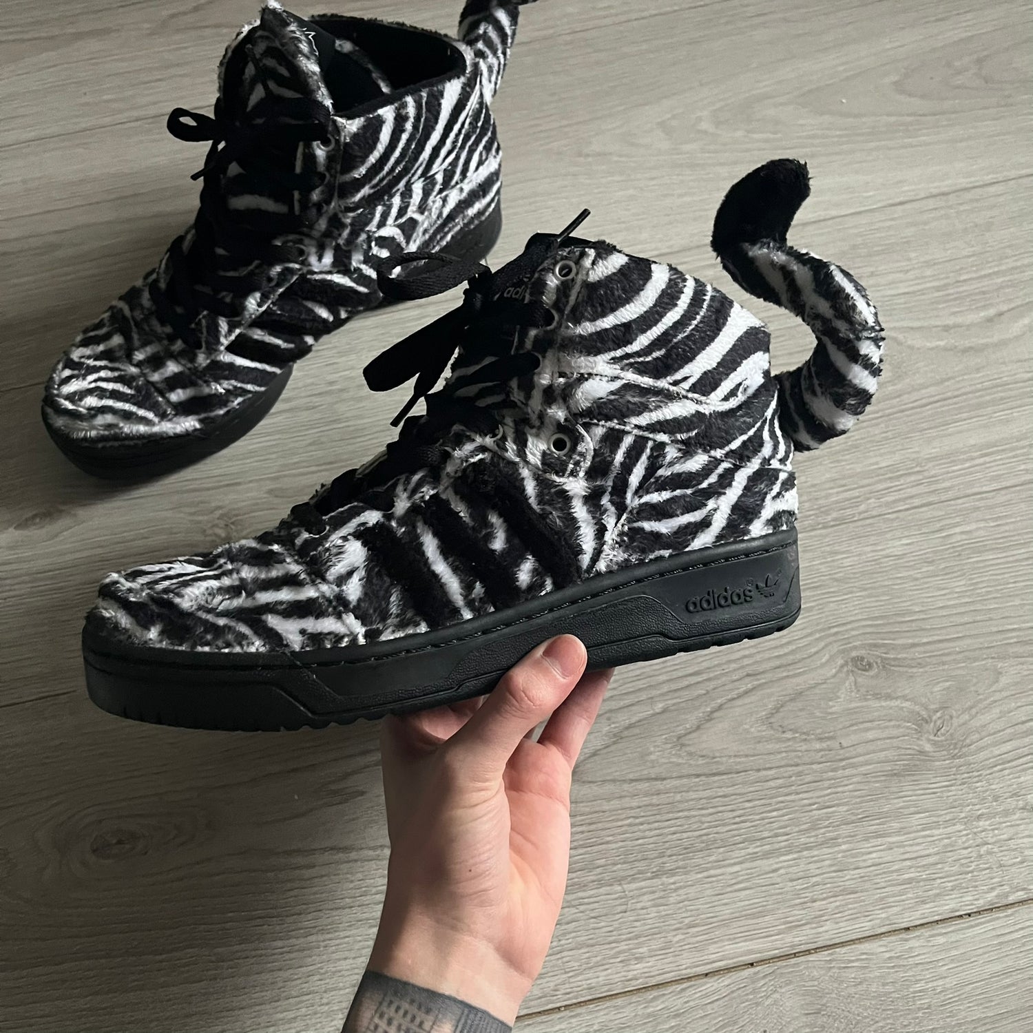 Adidas Jeremy Scott Zebra Black &amp; White Sneakers – Sample pair, Style G95749. High-top sneakers featuring black and white faux-fur zebra print, a 3D tail at the heel, rubber soles, and front lace closure. From the FW13 Jeremy Scott for Adidas collection, these iconic sneakers combine classic adidas design with signature crazy JS styling.&nbsp;