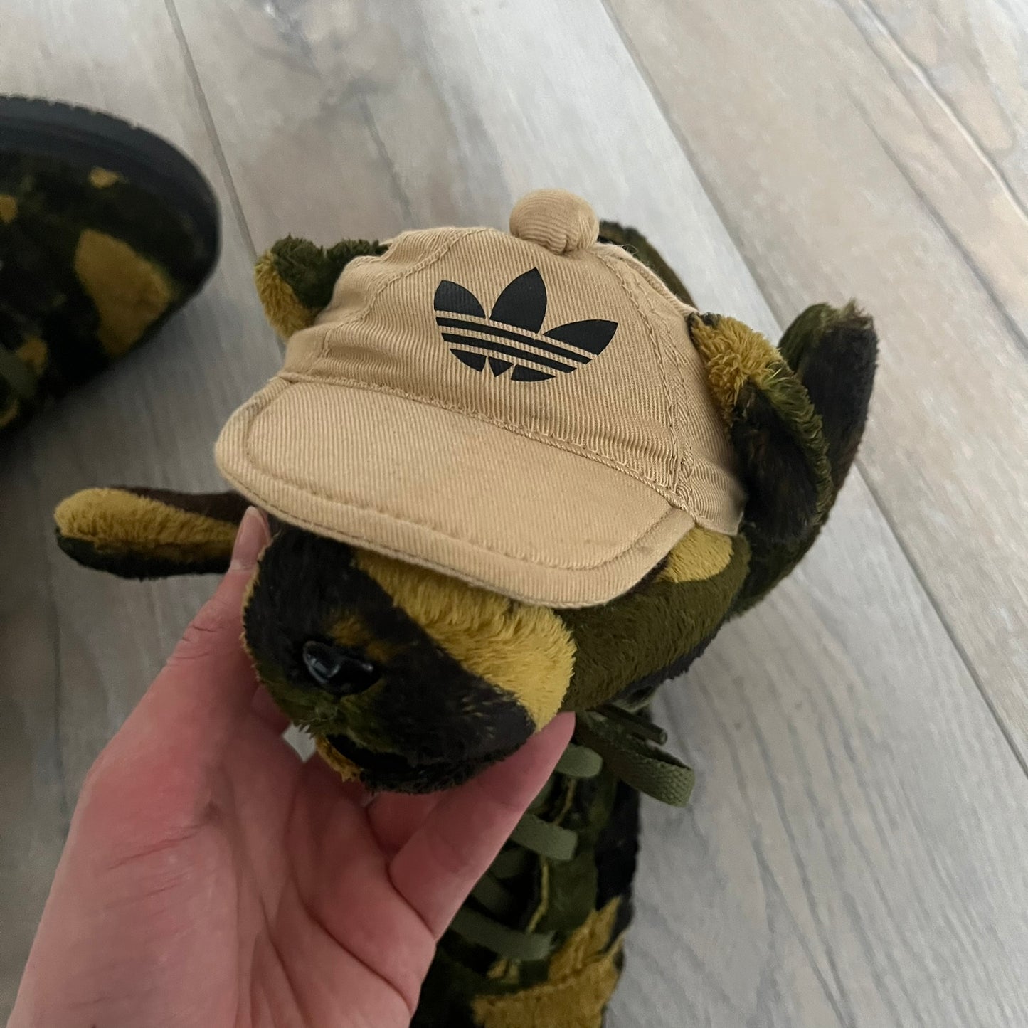 Adidas Jeremy Scott “Camo Bear” Sneakers (Style Q20917) released on March 16, 2013, in Earth Green/Black/Shioli. Featuring plush fleece uppers with a camouflage pattern, black three stripes, and a fully stuffed teddy bear head and arms on the tongue. Includes Jeremy Scott signature detailing on the inside heel and a black rubber sole.