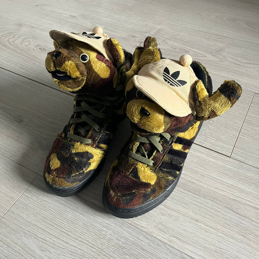 Adidas Jeremy Scott “Camo Bear” Sneakers (Style Q20917) released on March 16, 2013, in Earth Green/Black/Shioli. Featuring plush fleece uppers with a camouflage pattern, black three stripes, and a fully stuffed teddy bear head and arms on the tongue. Includes Jeremy Scott signature detailing on the inside heel and a black rubber sole.