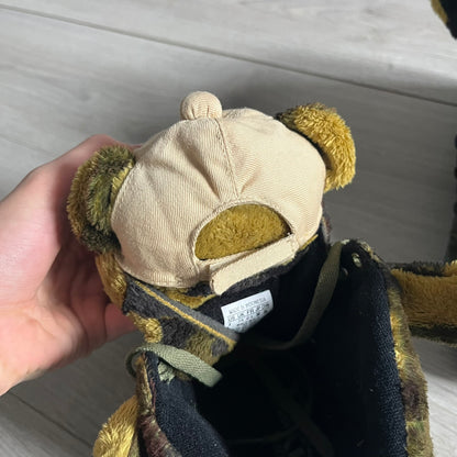 Adidas Jeremy Scott “Camo Bear” Sneakers (Style Q20917) released on March 16, 2013, in Earth Green/Black/Shioli. Featuring plush fleece uppers with a camouflage pattern, black three stripes, and a fully stuffed teddy bear head and arms on the tongue. Includes Jeremy Scott signature detailing on the inside heel and a black rubber sole.