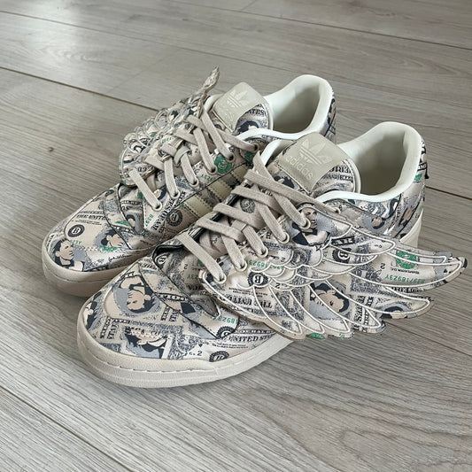 Adidas Jeremy Scott x Forum Wings 1.0 Low Money, style GX6393, in a Bliss/Off White/Bliss colorway. This pair features a textile upper covered in Jeremy Scott’s signature currency-themed graphic, swapping George Washington’s portrait for his own. The iconic 3D wings sit on the side of the shoe, with embossed adidas branding and Scott’s signature on opposite panels. Built with an EVA wedge for lightweight cushioning and a durable rubber cup sole. First released on October 21, 2021.