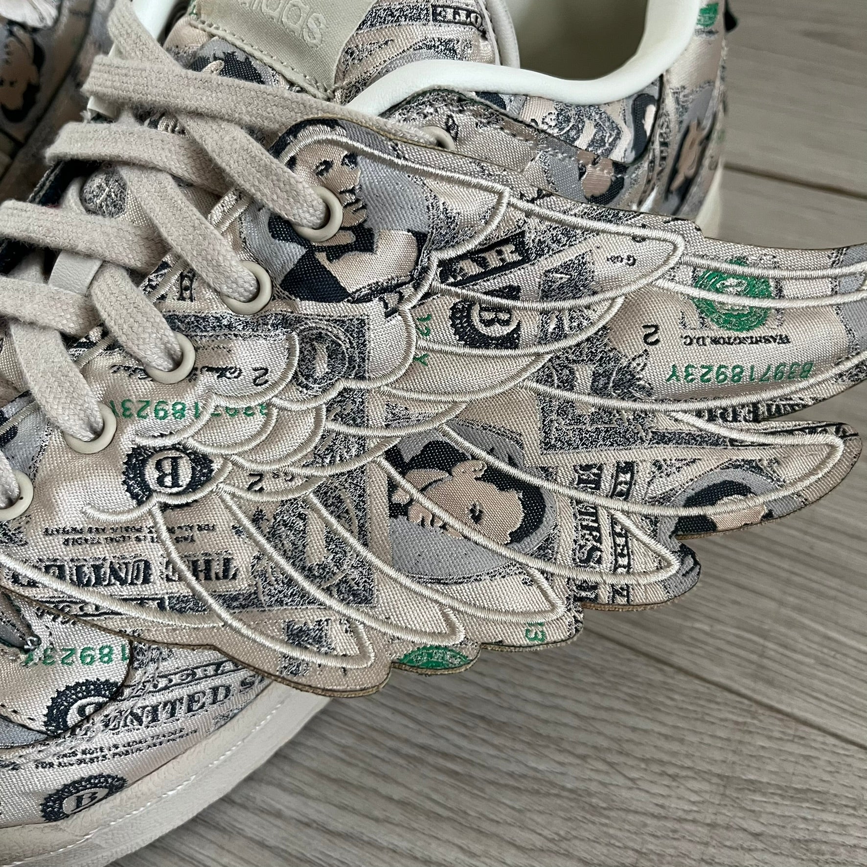 Adidas Jeremy Scott x Forum Wings 1.0 Low Money, style GX6393, in a Bliss/Off White/Bliss colorway. This pair features a textile upper covered in Jeremy Scott’s signature currency-themed graphic, swapping George Washington’s portrait for his own. The iconic 3D wings sit on the side of the shoe, with embossed adidas branding and Scott’s signature on opposite panels. Built with an EVA wedge for lightweight cushioning and a durable rubber cup sole. First released on October 21, 2021.