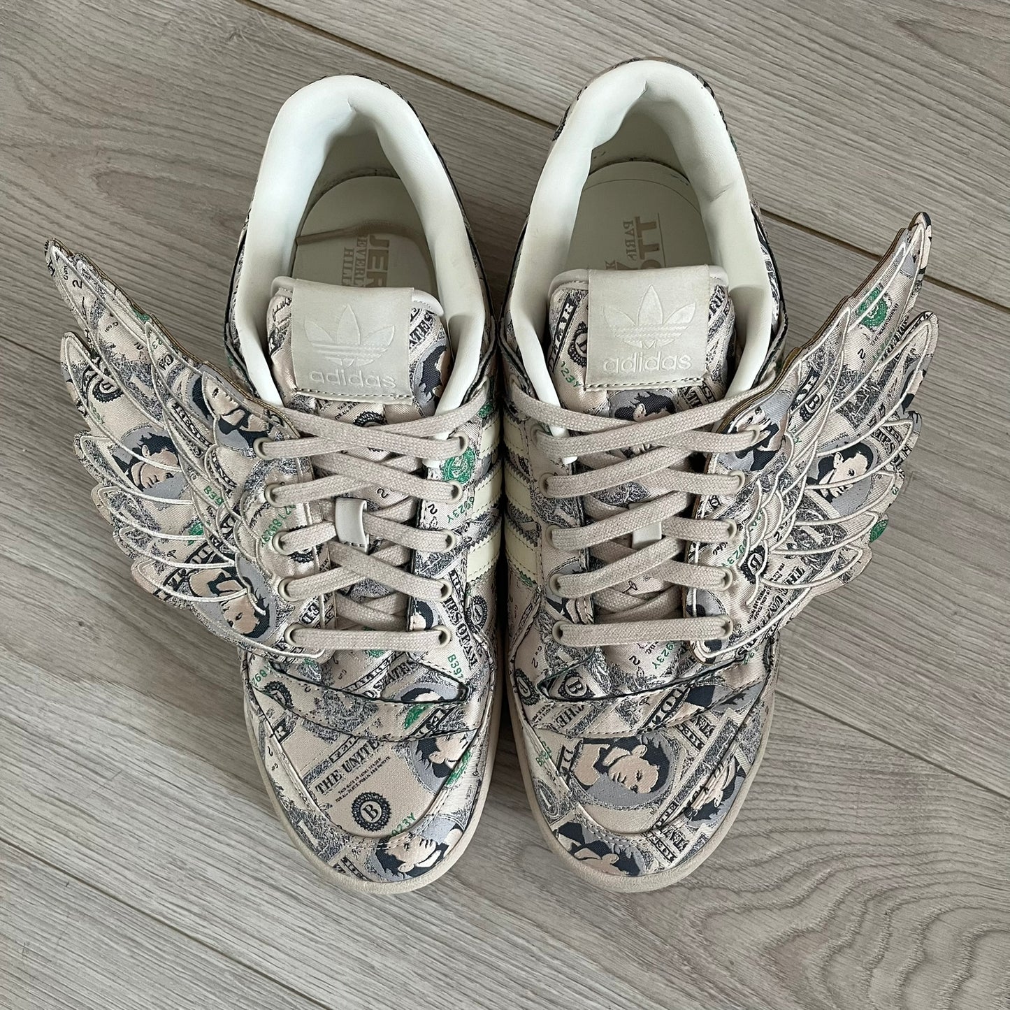 Adidas Jeremy Scott x Forum Wings 1.0 Low Money, style GX6393, in a Bliss/Off White/Bliss colorway. This pair features a textile upper covered in Jeremy Scott’s signature currency-themed graphic, swapping George Washington’s portrait for his own. The iconic 3D wings sit on the side of the shoe, with embossed adidas branding and Scott’s signature on opposite panels. Built with an EVA wedge for lightweight cushioning and a durable rubber cup sole. First released on October 21, 2021.