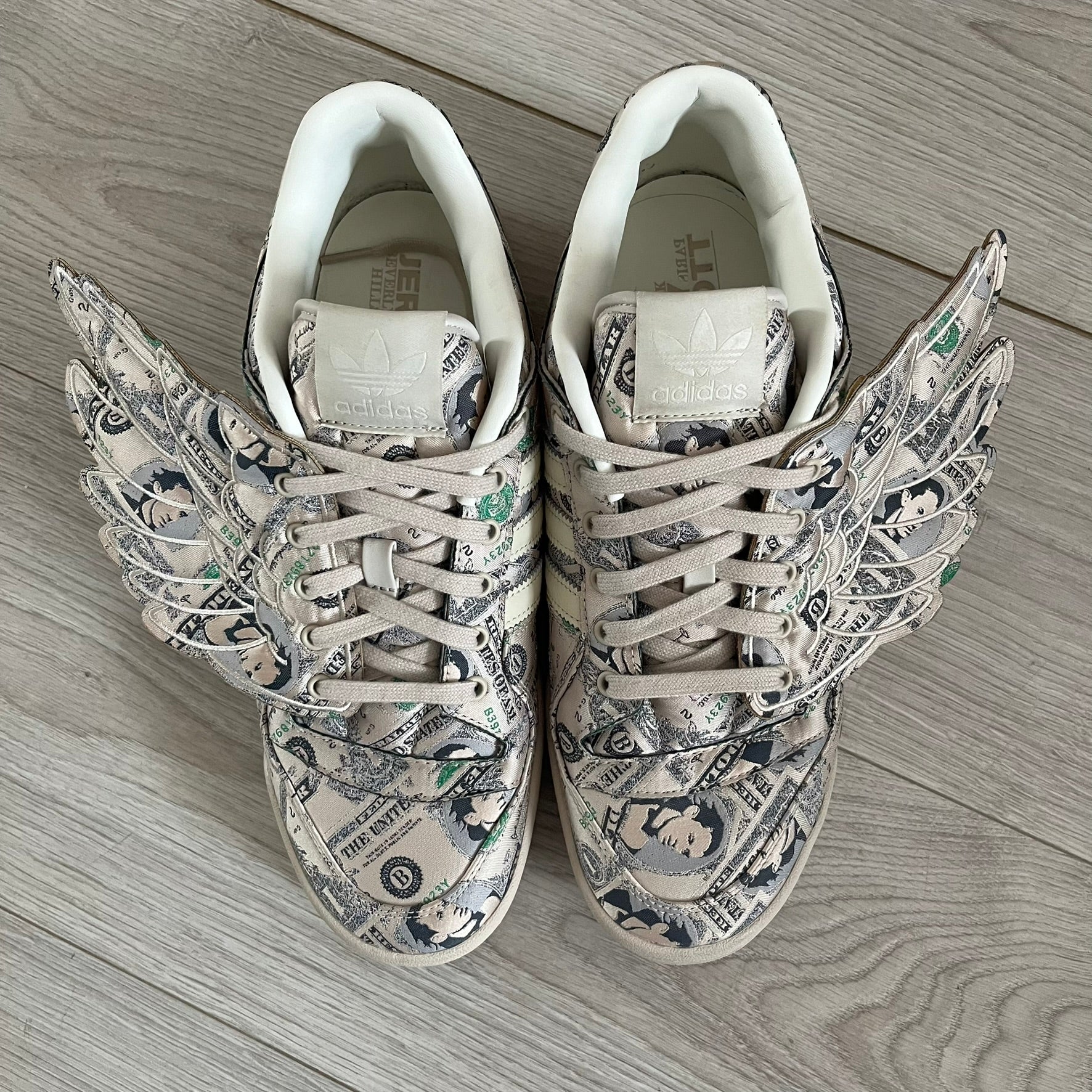 Adidas Jeremy Scott x Forum Wings 1.0 Low Money, style GX6393, in a Bliss/Off White/Bliss colorway. This pair features a textile upper covered in Jeremy Scott’s signature currency-themed graphic, swapping George Washington’s portrait for his own. The iconic 3D wings sit on the side of the shoe, with embossed adidas branding and Scott’s signature on opposite panels. Built with an EVA wedge for lightweight cushioning and a durable rubber cup sole. First released on October 21, 2021.