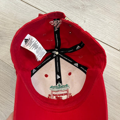 Adidas Liverpool 2007/08 Football Cap is a red cap featuring three white embroidered stripes across the front and an embroidered Liverpool crest at the center. The back is finished with a white embroidered Adidas logo and an adjustable metal clasp engraved with Liverpool detailing. Produced for the 2007/08 season