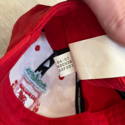 Adidas Liverpool 2007/08 Football Cap is a red cap featuring three white embroidered stripes across the front and an embroidered Liverpool crest at the center. The back is finished with a white embroidered Adidas logo and an adjustable metal clasp engraved with Liverpool detailing. Produced for the 2007/08 season