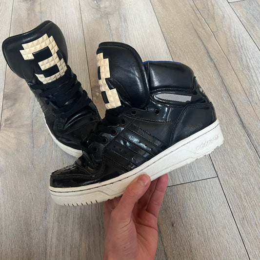 Adidas Originals 2013 M Attitude Logo Three Sneakers in black feature a leather and lacquer upper with a white rubber sole and blue interior lining. The tongue displays a large “3” made of small square details, and the heel has a trifold white adidas logo. Released in 2013, the Q23025 model highlights the M Attitude line design.