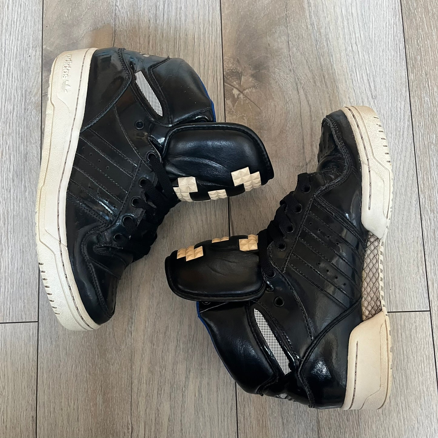 Adidas Originals 2013 M Attitude Logo Three Sneakers in black feature a leather and lacquer upper with a white rubber sole and blue interior lining. The tongue displays a large “3” made of small square details, and the heel has a trifold white adidas logo. Released in 2013, the Q23025 model highlights the M Attitude line design.