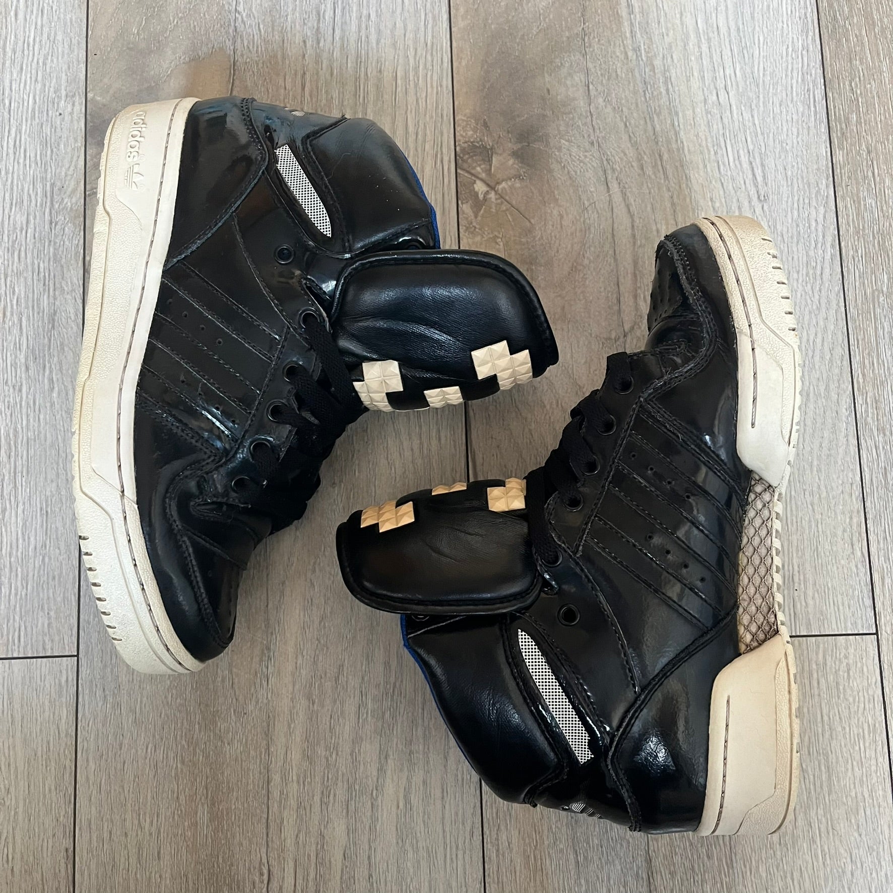 Adidas Originals 2013 M Attitude Logo Three Sneakers in black feature a leather and lacquer upper with a white rubber sole and blue interior lining. The tongue displays a large “3” made of small square details, and the heel has a trifold white adidas logo. Released in 2013, the Q23025 model highlights the M Attitude line design.