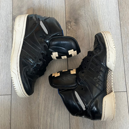 Adidas Originals 2013 M Attitude Logo Three Sneakers in black feature a leather and lacquer upper with a white rubber sole and blue interior lining. The tongue displays a large “3” made of small square details, and the heel has a trifold white adidas logo. Released in 2013, the Q23025 model highlights the M Attitude line design.