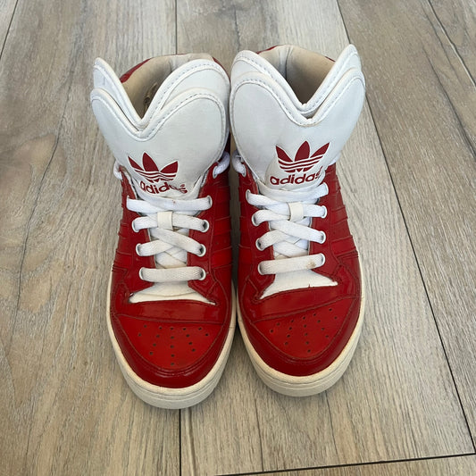 Adidas Originals Metro Attitude Logo Heart Sneakers are women’s sneakers released in 2012, featuring a red suede upper with matching University-Red accents. The design includes dual heart-shaped tongues in white with red Adidas logos, paired with a white sole and laces. Metro Attitude Logo Heart W model (G61014) inspired by Jeremy Scott collaborations.