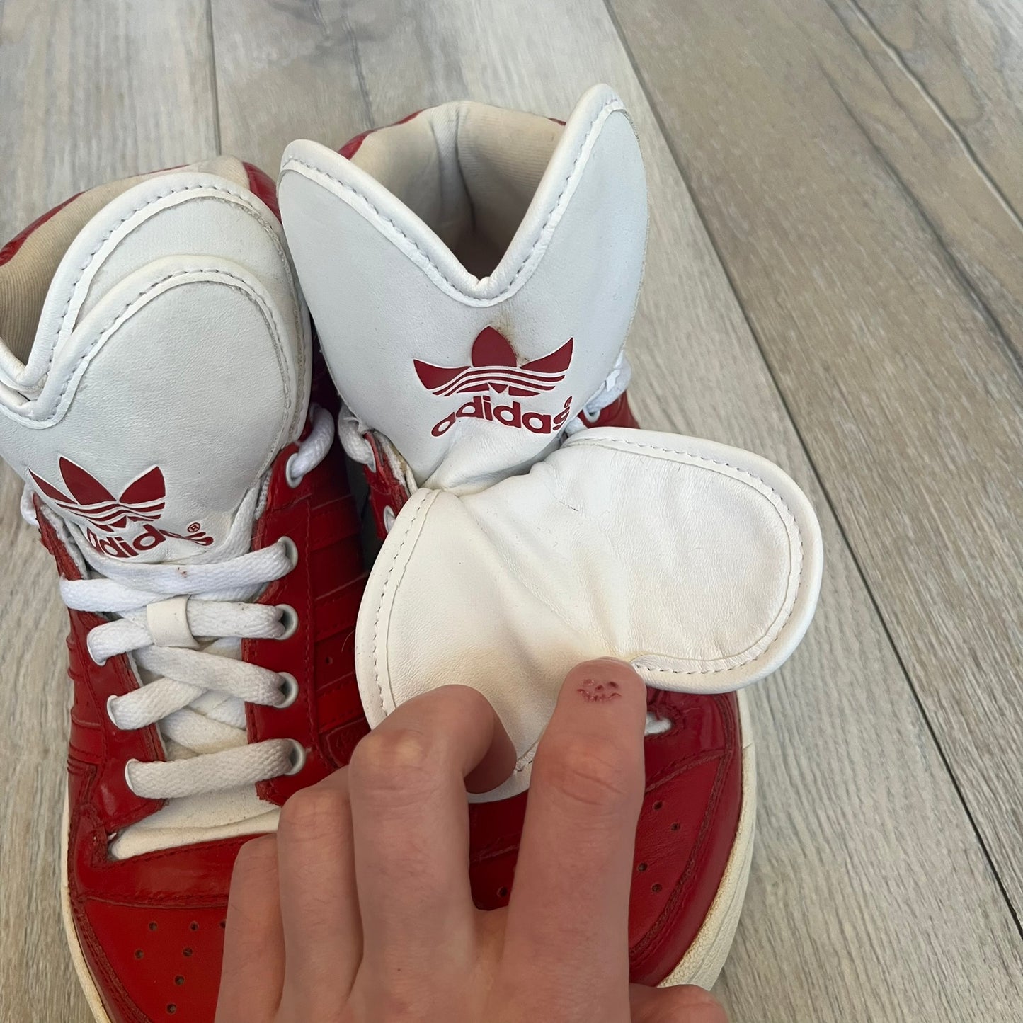 Adidas Originals Metro Attitude Logo Heart Sneakers are women’s sneakers released in 2012, featuring a red suede upper with matching University-Red accents. The design includes dual heart-shaped tongues in white with red Adidas logos, paired with a white sole and laces. Metro Attitude Logo Heart W model (G61014) inspired by Jeremy Scott collaborations.