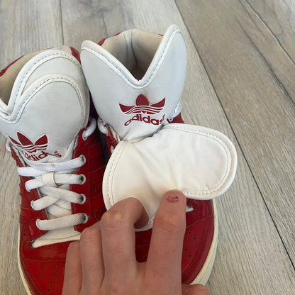 Adidas Originals Metro Attitude Logo Heart Sneakers are women’s sneakers released in 2012, featuring a red suede upper with matching University-Red accents. The design includes dual heart-shaped tongues in white with red Adidas logos, paired with a white sole and laces. Metro Attitude Logo Heart W model (G61014) inspired by Jeremy Scott collaborations.