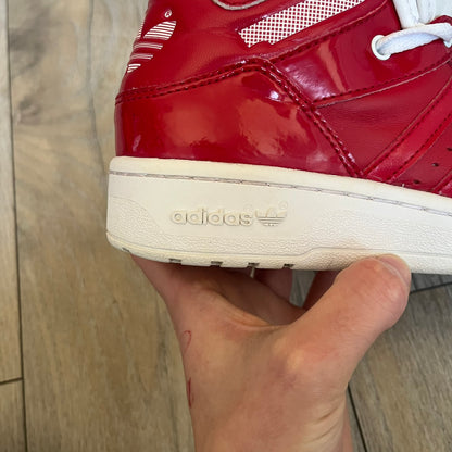 Adidas Originals Metro Attitude Logo Heart Sneakers are women’s sneakers released in 2012, featuring a red suede upper with matching University-Red accents. The design includes dual heart-shaped tongues in white with red Adidas logos, paired with a white sole and laces. Metro Attitude Logo Heart W model (G61014) inspired by Jeremy Scott collaborations.
