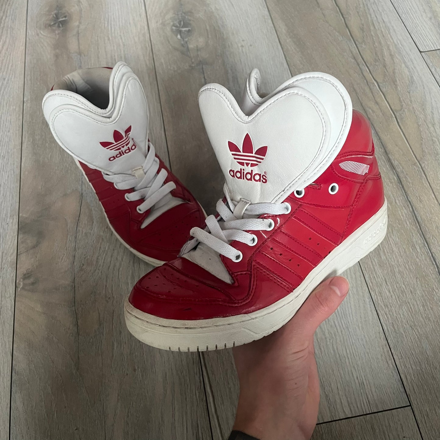 Adidas Originals Metro Attitude Logo Heart Sneakers are women’s sneakers released in 2012, featuring a red suede upper with matching University-Red accents. The design includes dual heart-shaped tongues in white with red Adidas logos, paired with a white sole and laces. Metro Attitude Logo Heart W model (G61014) inspired by Jeremy Scott collaborations.