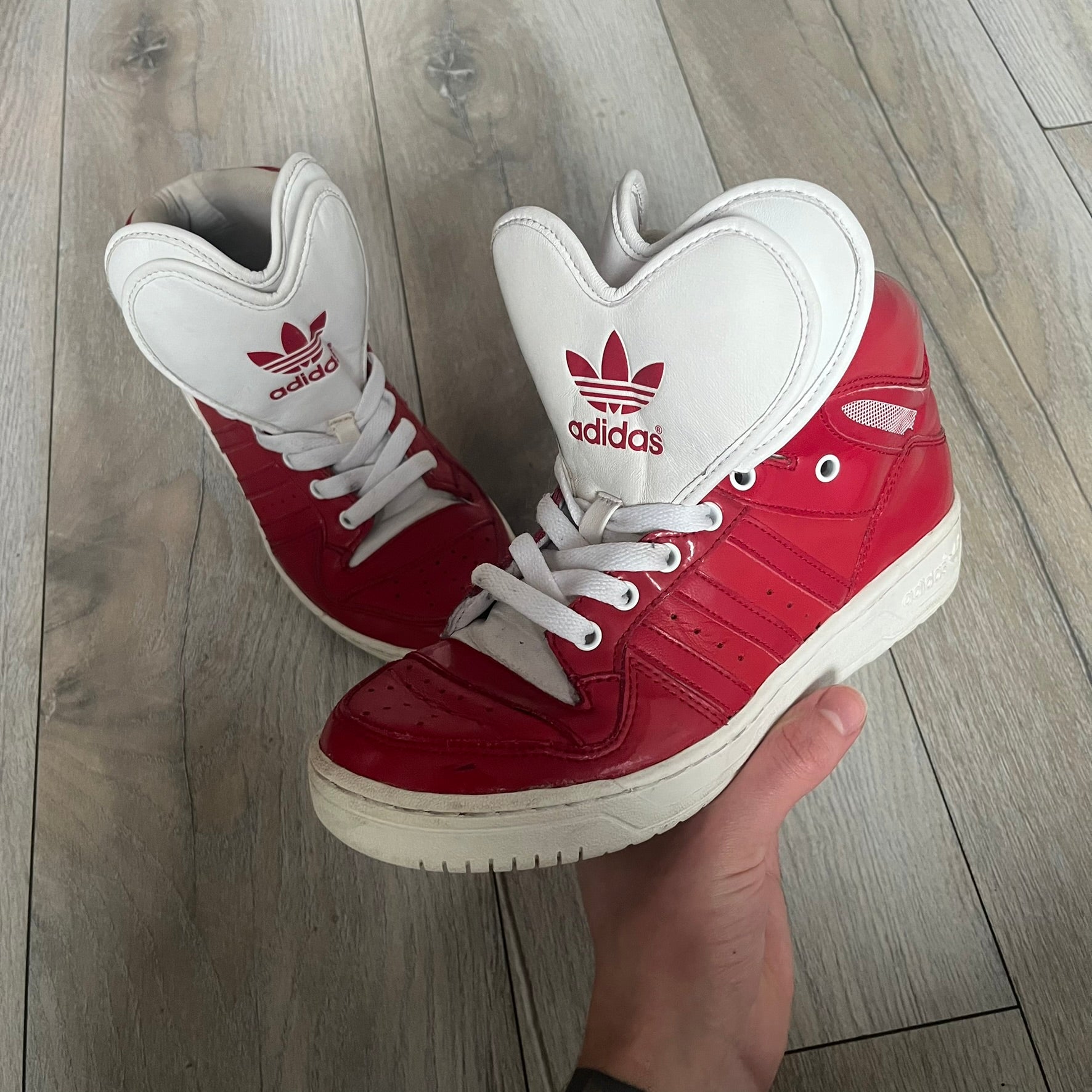 Adidas Originals Metro Attitude Logo Heart Sneakers are women’s sneakers released in 2012, featuring a red suede upper with matching University-Red accents. The design includes dual heart-shaped tongues in white with red Adidas logos, paired with a white sole and laces. Metro Attitude Logo Heart W model (G61014) inspired by Jeremy Scott collaborations.