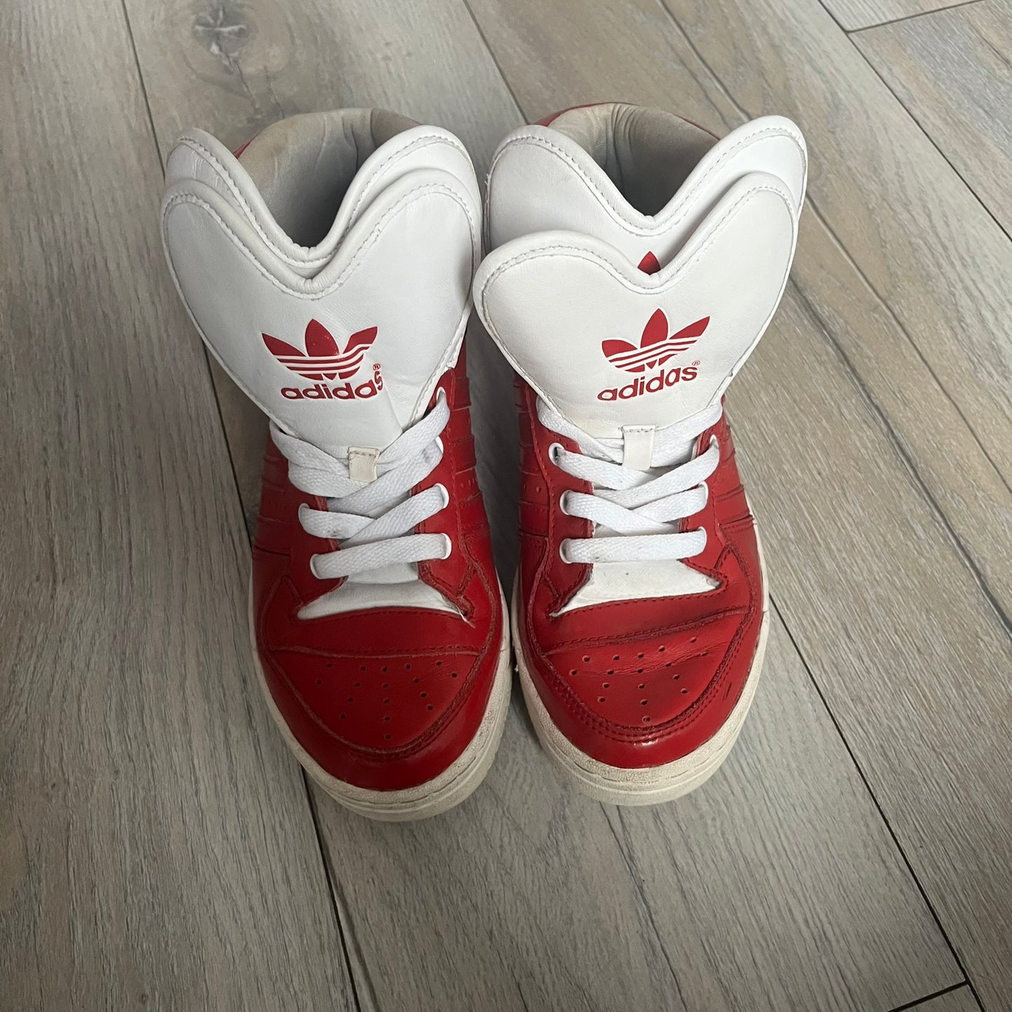 Adidas Originals Metro Attitude Logo Heart Sneakers are women’s sneakers released in 2012, featuring a red suede upper with matching University-Red accents. The design includes dual heart-shaped tongues in white with red Adidas logos, paired with a white sole and laces. Metro Attitude Logo Heart W model (G61014) inspired by Jeremy Scott collaborations.