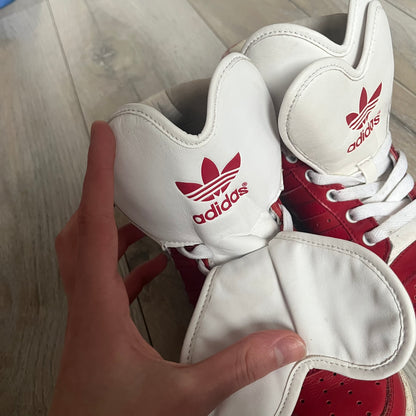 Adidas Originals Metro Attitude Logo Heart Sneakers are women’s sneakers released in 2012, featuring a red suede upper with matching University-Red accents. The design includes dual heart-shaped tongues in white with red Adidas logos, paired with a white sole and laces. Metro Attitude Logo Heart W model (G61014) inspired by Jeremy Scott collaborations.