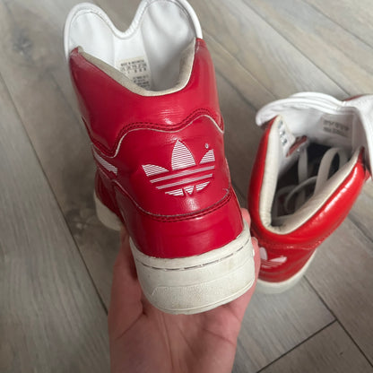 Adidas Originals Metro Attitude Logo Heart Sneakers are women’s sneakers released in 2012, featuring a red suede upper with matching University-Red accents. The design includes dual heart-shaped tongues in white with red Adidas logos, paired with a white sole and laces. Metro Attitude Logo Heart W model (G61014) inspired by Jeremy Scott collaborations.