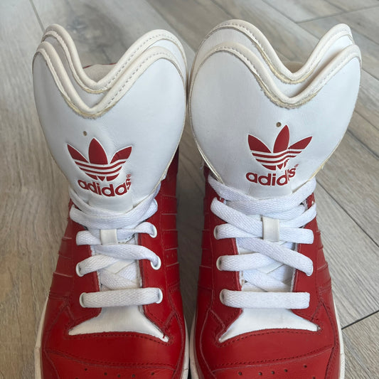 Adidas Originals Metro Attitude Logo Heart Sneakers are women’s sneakers released in 2012, featuring a red suede upper with matching University-Red accents. The design includes dual heart-shaped tongues in white with red Adidas logos, paired with a white sole and laces. Metro Attitude Logo Heart W model (G61014) inspired by Jeremy Scott collaborations