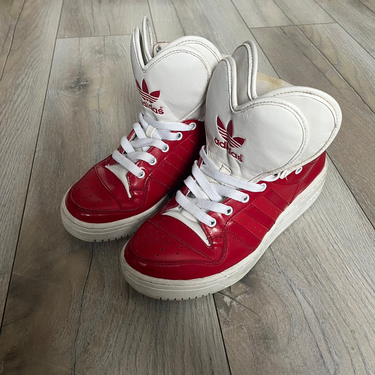 Adidas Originals Metro Attitude Logo Heart Sneakers are women’s sneakers released in 2012, featuring a red suede upper with matching University-Red accents. The design includes dual heart-shaped tongues in white with red Adidas logos, paired with a white sole and laces. Metro Attitude Logo Heart W model (G61014) inspired by Jeremy Scott collaborations.
