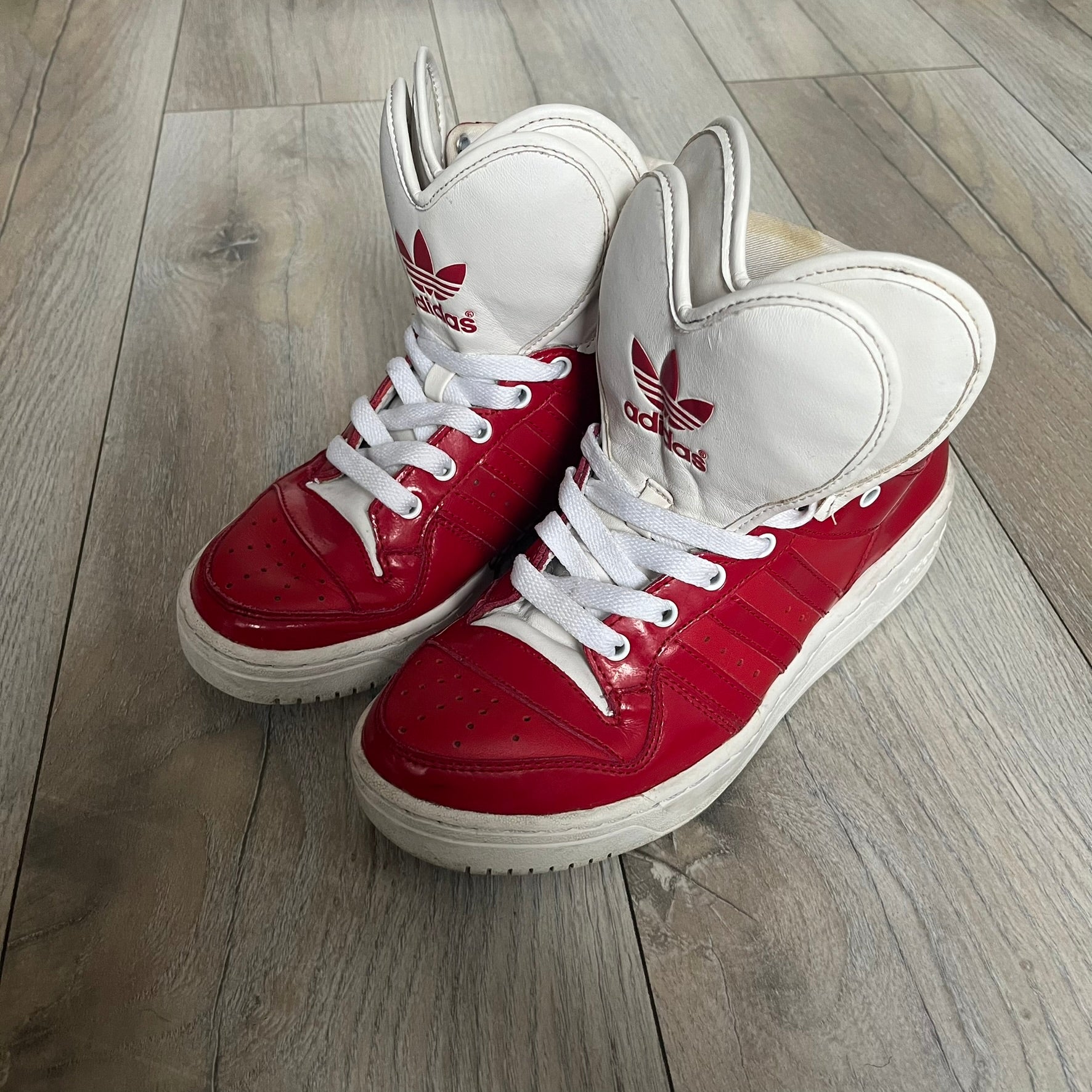 Adidas Originals Metro Attitude Logo Heart Sneakers are women’s sneakers released in 2012, featuring a red suede upper with matching University-Red accents. The design includes dual heart-shaped tongues in white with red Adidas logos, paired with a white sole and laces. Metro Attitude Logo Heart W model (G61014) inspired by Jeremy Scott collaborations.