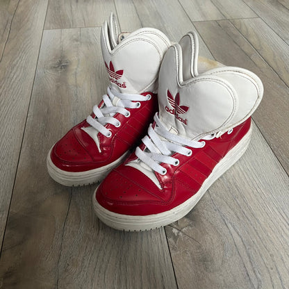 Adidas Originals Metro Attitude Logo Heart Sneakers are women’s sneakers released in 2012, featuring a red suede upper with matching University-Red accents. The design includes dual heart-shaped tongues in white with red Adidas logos, paired with a white sole and laces. Metro Attitude Logo Heart W model (G61014) inspired by Jeremy Scott collaborations.