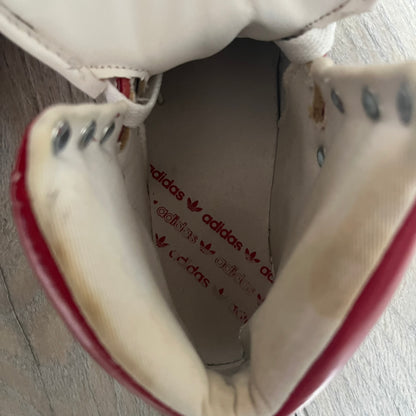 Adidas Originals Metro Attitude Logo Heart Sneakers are women’s sneakers released in 2012, featuring a red suede upper with matching University-Red accents. The design includes dual heart-shaped tongues in white with red Adidas logos, paired with a white sole and laces. Metro Attitude Logo Heart W model (G61014) inspired by Jeremy Scott collaborations.