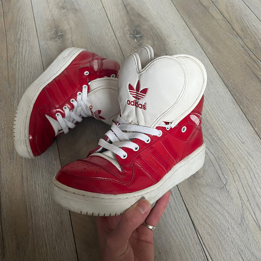 Adidas Originals Metro Attitude Logo Heart Sneakers are women’s sneakers released in 2012, featuring a red suede upper with matching University-Red accents. The design includes dual heart-shaped tongues in white with red Adidas logos, paired with a white sole and laces. Metro Attitude Logo Heart W model (G61014) inspired by Jeremy Scott collaborations.