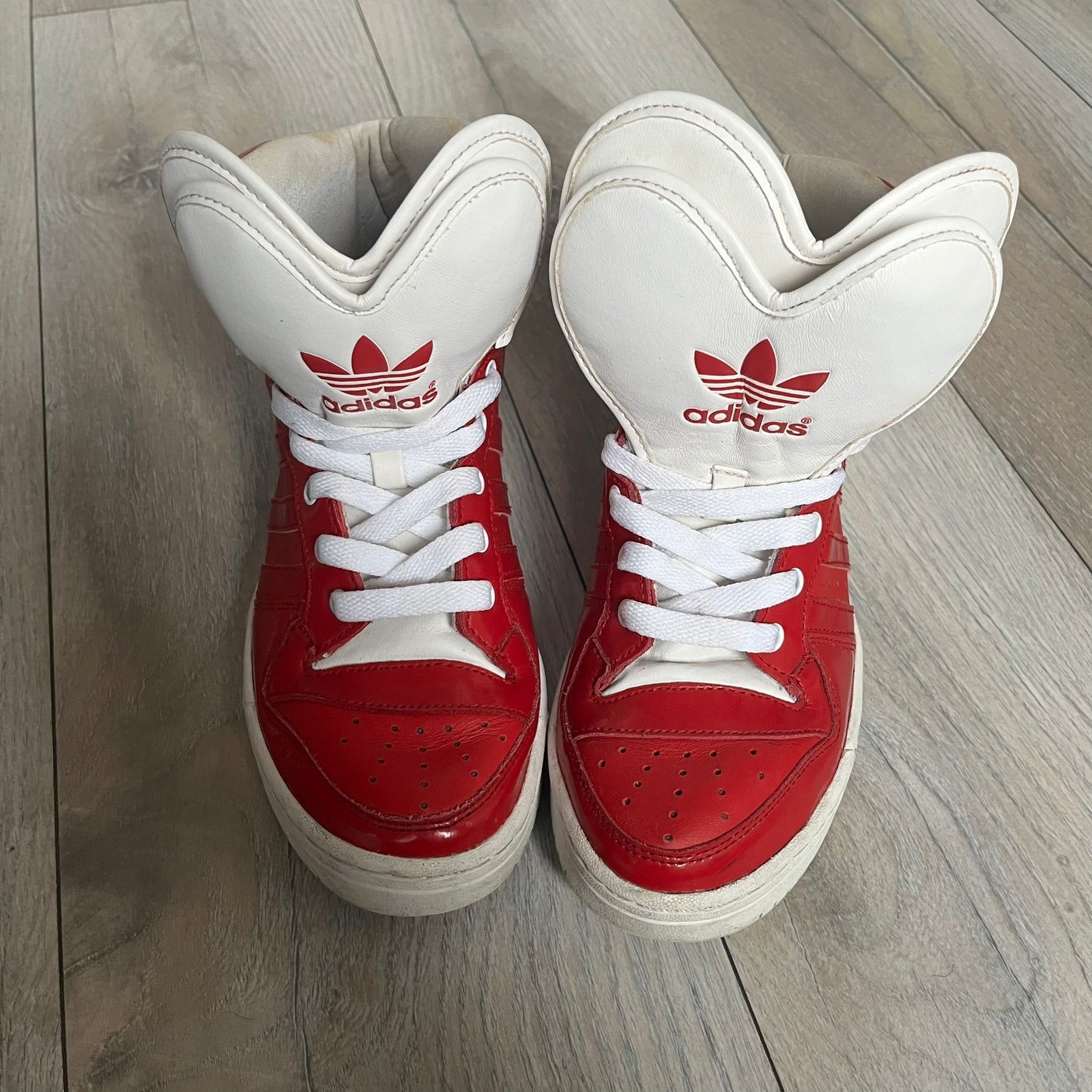 Adidas Originals Metro Attitude Logo Heart Sneakers are women’s sneakers released in 2012, featuring a red suede upper with matching University-Red accents. The design includes dual heart-shaped tongues in white with red Adidas logos, paired with a white sole and laces. Metro Attitude Logo Heart W model (G61014) inspired by Jeremy Scott collaborations.