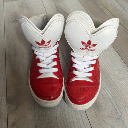 Adidas Originals Metro Attitude Logo Heart Sneakers are women’s sneakers released in 2012, featuring a red suede upper with matching University-Red accents. The design includes dual heart-shaped tongues in white with red Adidas logos, paired with a white sole and laces. Metro Attitude Logo Heart W model (G61014) inspired by Jeremy Scott collaborations.