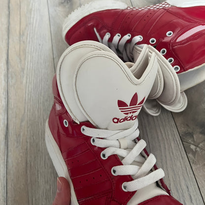 Adidas Originals Metro Attitude Logo Heart Sneakers are women’s sneakers released in 2012, featuring a red suede upper with matching University-Red accents. The design includes dual heart-shaped tongues in white with red Adidas logos, paired with a white sole and laces. Metro Attitude Logo Heart W model (G61014) inspired by Jeremy Scott collaborations.