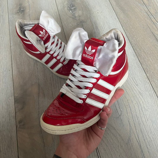 Adidas Originals Top Ten Hi Sleek Bow Sneakers are women’s high-top sneakers in University-Red and white leather. They feature a removable white bow on the tongue, white Adidas stripes, laces, and a white sole. Released under product number G61361, the sneakers include patent leather details for a polished finish.