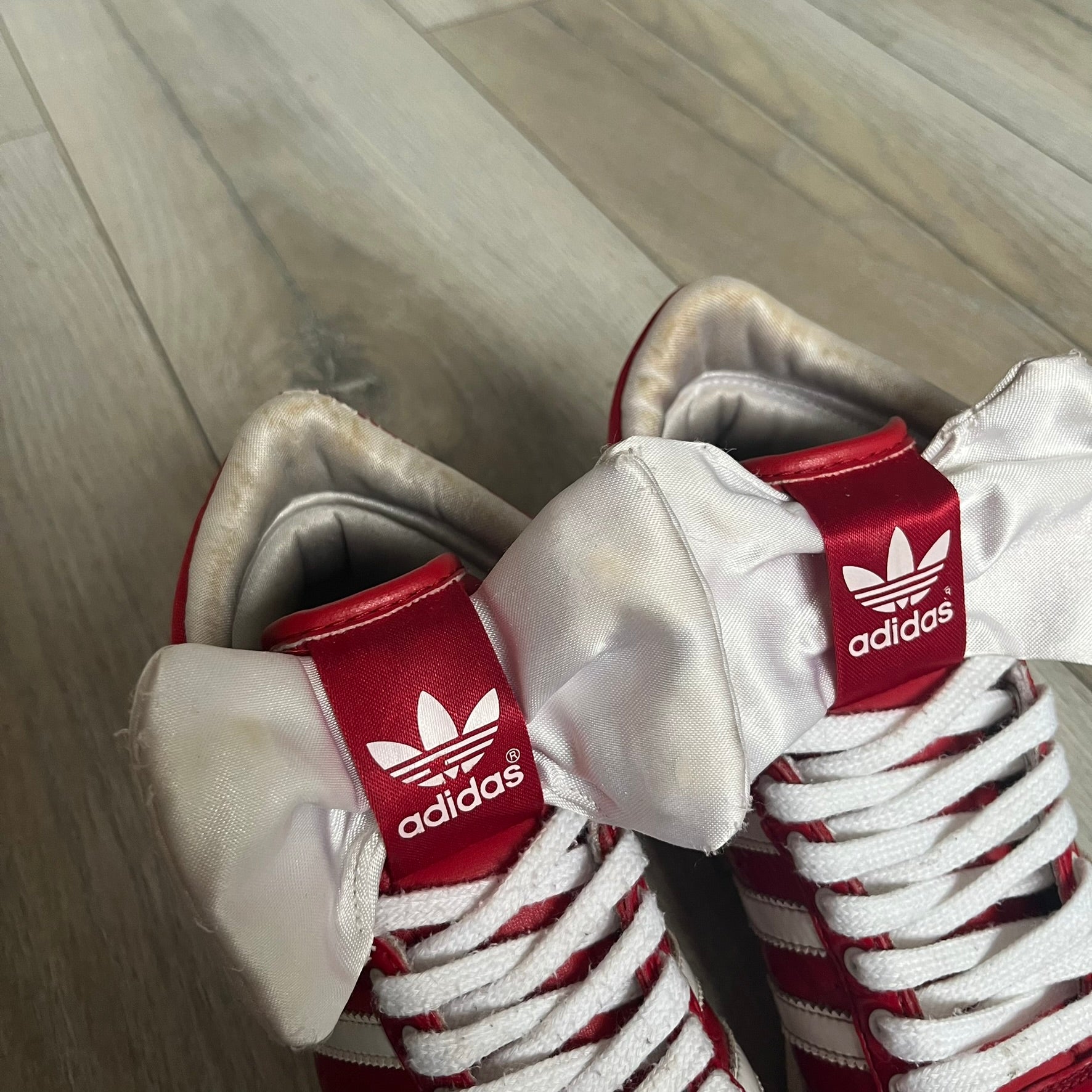 Adidas Originals Top Ten Hi Sleek Bow Sneakers are women’s high-top sneakers in University-Red and white leather. They feature a removable white bow on the tongue, white Adidas stripes, laces, and a white sole. Released under product number G61361, the sneakers include patent leather details for a polished finish.