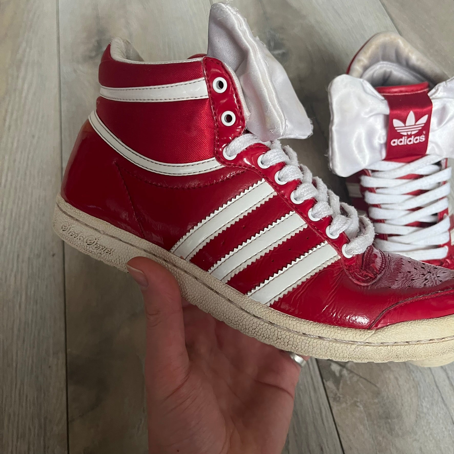 Adidas Originals Top Ten Hi Sleek Bow Sneakers are women’s high-top sneakers in University-Red and white leather. They feature a removable white bow on the tongue, white Adidas stripes, laces, and a white sole. Released under product number G61361, the sneakers include patent leather details for a polished finish.