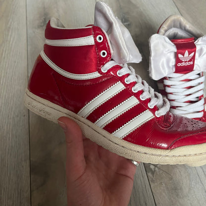Adidas Originals Top Ten Hi Sleek Bow Sneakers are women’s high-top sneakers in University-Red and white leather. They feature a removable white bow on the tongue, white Adidas stripes, laces, and a white sole. Released under product number G61361, the sneakers include patent leather details for a polished finish.