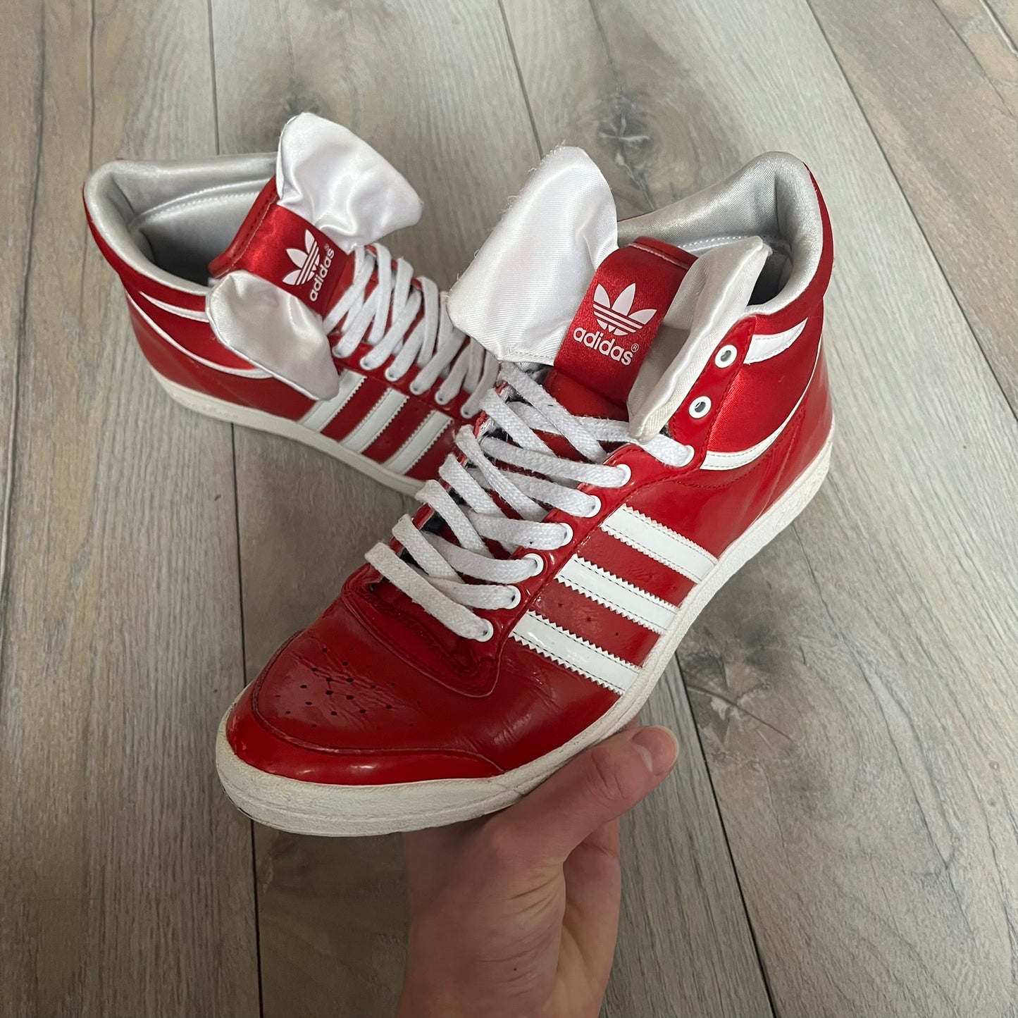 Adidas Originals Top Ten Hi Sleek Bow Sneakers are women’s high-top sneakers in University-Red and white leather. They feature a removable white bow on the tongue, white Adidas stripes, laces, and a white sole. Released under product number G61361, the sneakers include patent leather details for a polished finish.