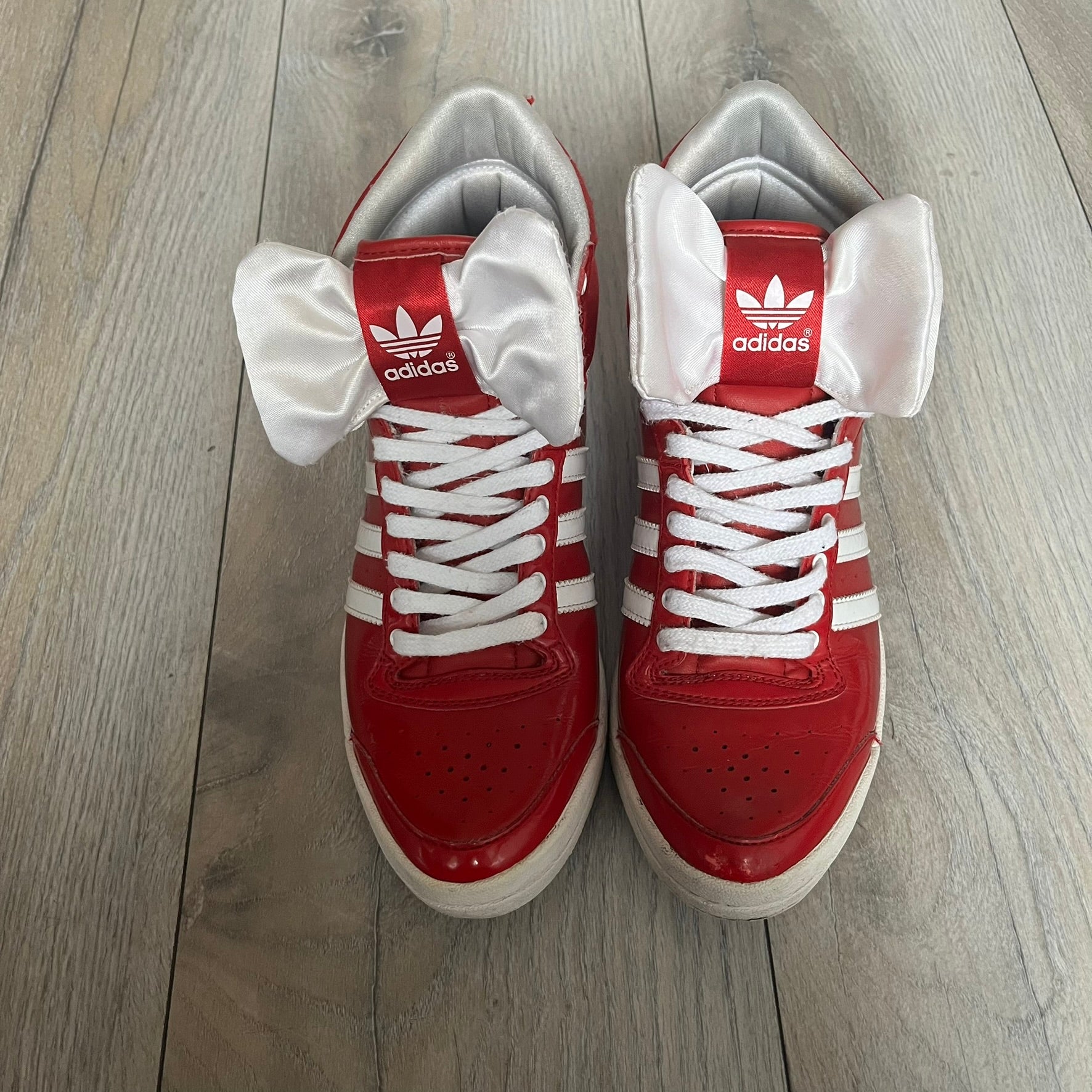 Adidas Originals Top Ten Hi Sleek Bow Sneakers are women’s high-top sneakers in University-Red and white leather. They feature a removable white bow on the tongue, white Adidas stripes, laces, and a white sole. Released under product number G61361, the sneakers include patent leather details for a polished finish.