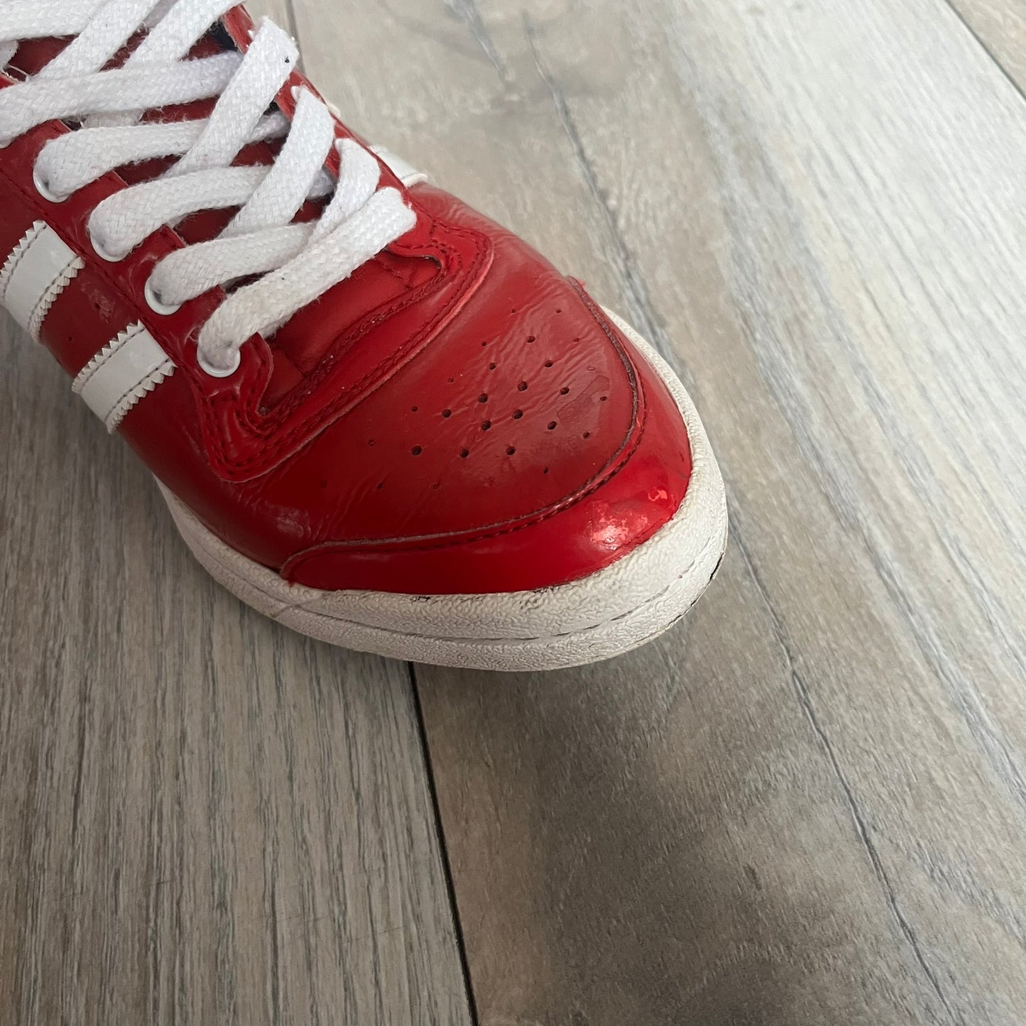 Adidas Originals Top Ten Hi Sleek Bow Sneakers are women’s high-top sneakers in University-Red and white leather. They feature a removable white bow on the tongue, white Adidas stripes, laces, and a white sole. Released under product number G61361, the sneakers include patent leather details for a polished finish.