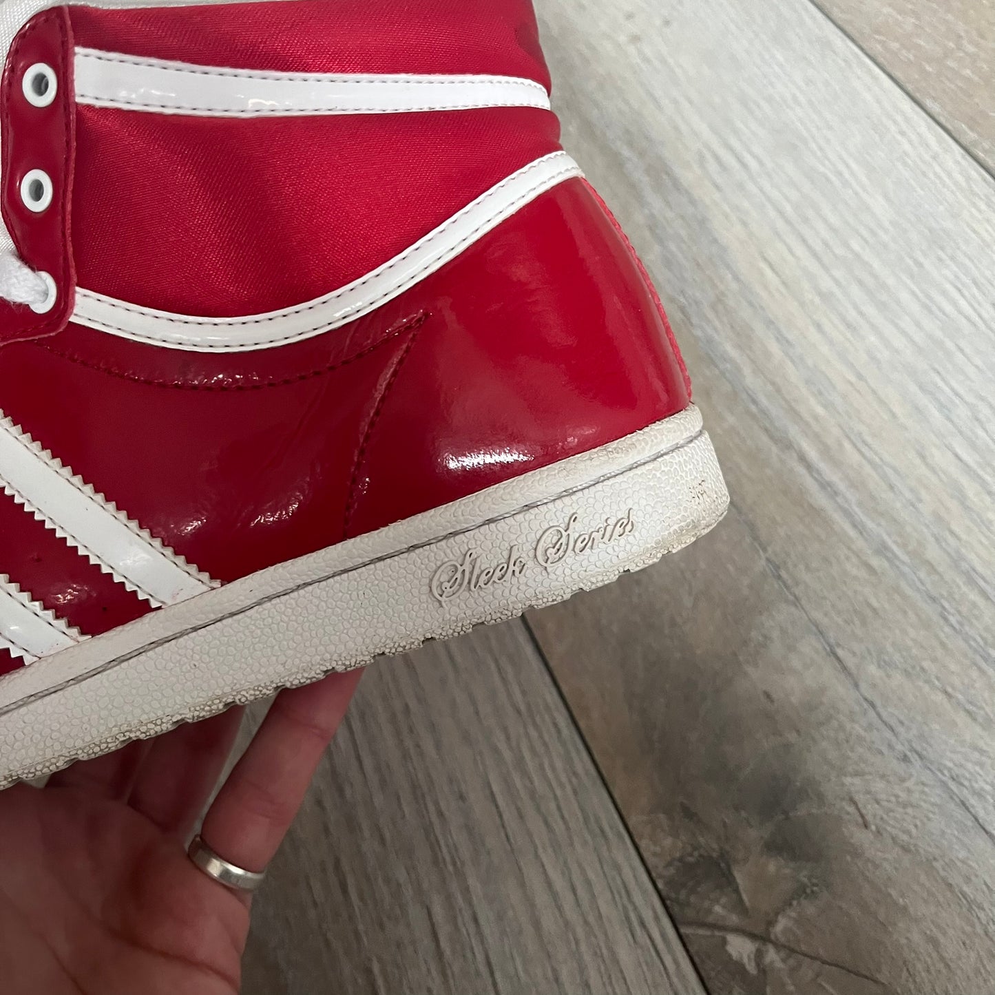 Adidas Originals Top Ten Hi Sleek Bow Sneakers are women’s high-top sneakers in University-Red and white leather. They feature a removable white bow on the tongue, white Adidas stripes, laces, and a white sole. Released under product number G61361, the sneakers include patent leather details for a polished finish.