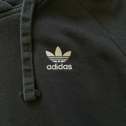 Adidas Trefoil Zip Pouch Hoodie in black, crafted from soft cotton for durability and comfort. Features a large Trefoil logo on the back within a circle, a smaller embroidered logo on the left chest, and a front zip pouch pocket. Designed with thick drawstrings and reinforced stitching, offering a sturdy, well-constructed fit.
