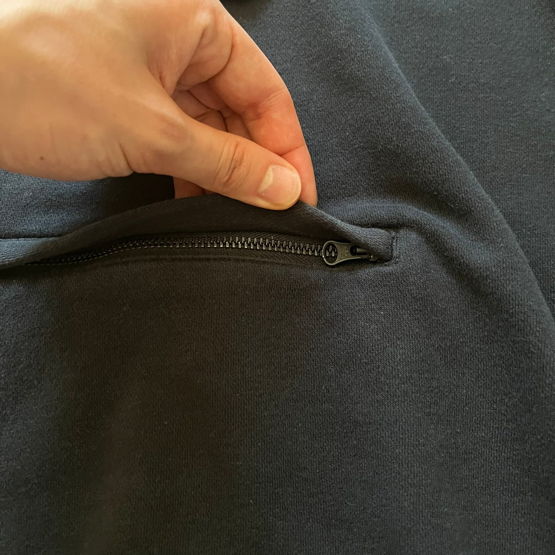 Adidas Trefoil Zip Pouch Hoodie in black, crafted from soft cotton for durability and comfort. Features a large Trefoil logo on the back within a circle, a smaller embroidered logo on the left chest, and a front zip pouch pocket. Designed with thick drawstrings and reinforced stitching, offering a sturdy, well-constructed fit.